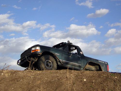 1995 Ford Bronco with aftermarket bumper and roof lights on a dirt mound under a cloudy sky