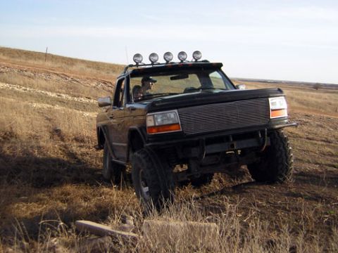 1995 Ford Bronco - Black lifted full-size Ford Bronco with its top removed, parked in a dry prairie field and shot from the front three-quarter. It carries a…