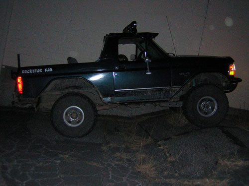 Dark green Ford Bronco with "ROCKSTAR FAB" on the side, parked on uneven ground