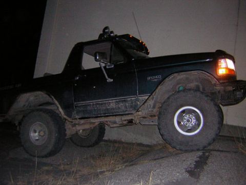 1995 Ford Bronco - A dark green Ford Bronco is angled on a rocky surface, with its front right tire elevated.