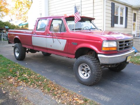1979 Ford Bronco - This red crew cab pickup truck is parked in a driveway with a house in the background.