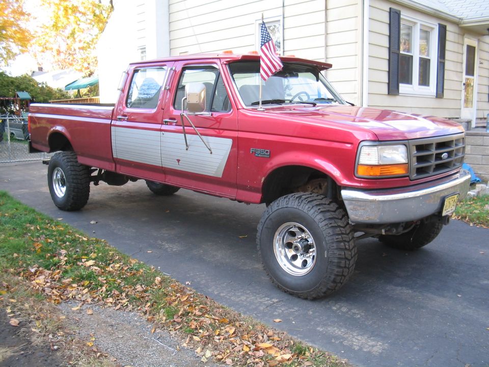 Lifted red two-tone Ford F-350 crew cab 4x4 with mud tires in a driveway