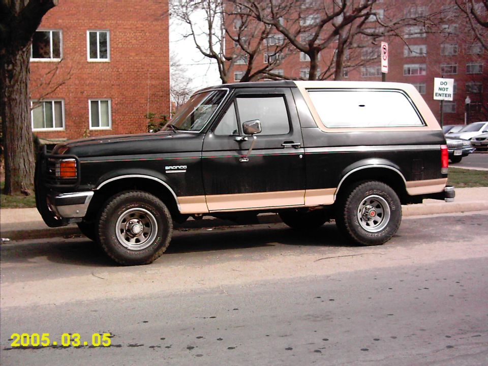 Black two-door Ford Bronco SUV with tan trim shown in side profile parked at a curb