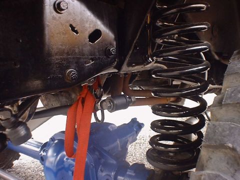 1988 Ford Bronco - Close-up view of vehicle suspension parts, including a coil spring and a blue differential, with a red strap attached.