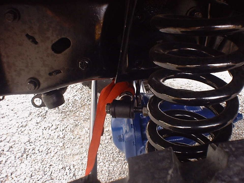 Close-up of a vehicle's suspension with a blue component and an orange strap around a black rod