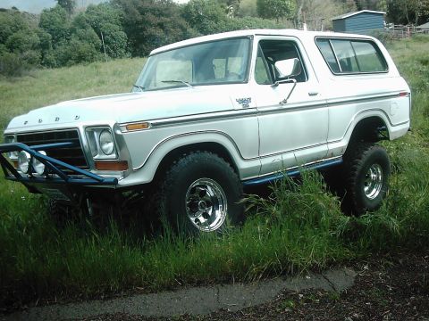 1978 Ford Bronco - A white 1978 Ford Bronco is shown from a 3/4 front angle, equipped with a blue brush guard and off-road tires.