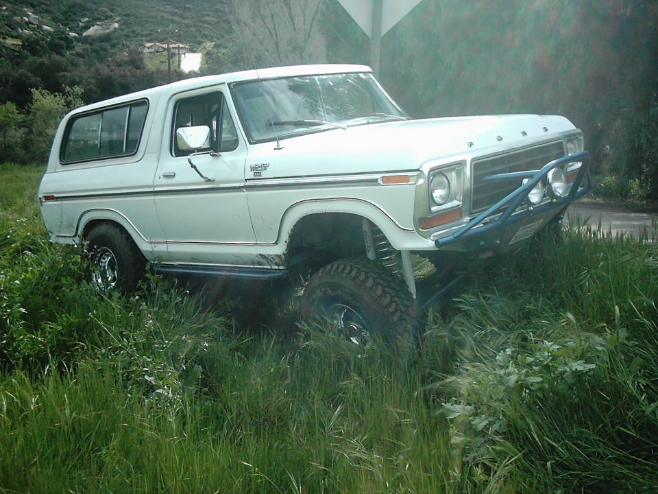 White 1978 Ford Bronco with blue off-road bumper and large tires