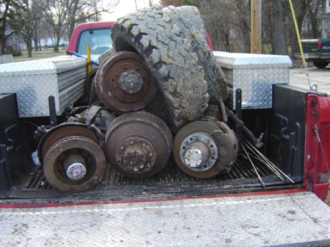 1992 Ford Bronco - A red pickup truck bed is filled with various brake components and a large, dirty tire, suggesting a repair or parts haul.