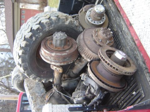 1992 Ford Bronco - Various rusty truck axle components and a tire are piled in the bed of a pickup truck.