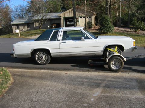 1985 Ford Crown Victoria LTD - A white two-door sedan is loaded onto a trailer, ready for transport. The vehicle appears to be from the mid-1980s.