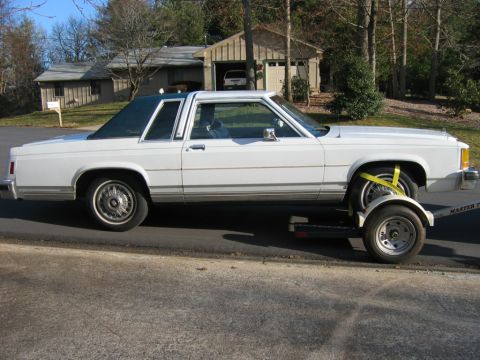 1985 Ford Crown Victoria LTD - A white two-door sedan is being transported on a trailer, viewed from the side.