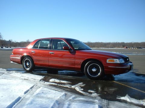 1999 Ford Crown Victoria - A red sedan is parked on a wet asphalt lot with snow on the ground under a clear blue sky.