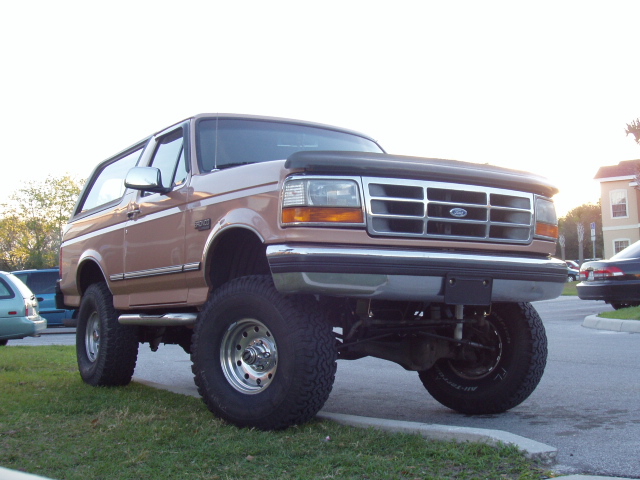 Tan lifted two-door Ford Bronco SUV on big off-road tires, 3/4 front view