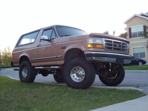 1994 Ford Bronco - This lifted 1994 Ford Bronco is shown in a 3/4 front view, parked on a grassy area next to a street.