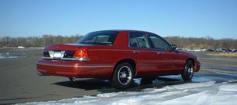 1999 Ford Crown Victoria - A red sedan is viewed from the rear quarter angle on a cold day.