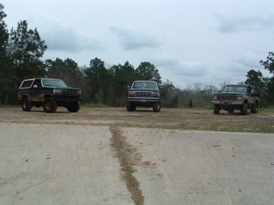 Three SUVs parked on a dirt lot, the leftmost is a dark 1992 Ford Bronco with mud on its body