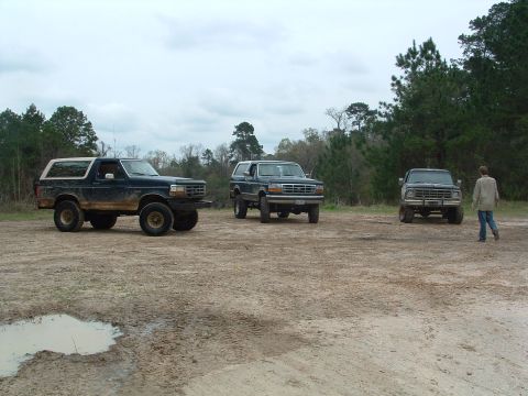 1993 Ford Bronco - Three Ford Broncos are parked in a muddy outdoor area with trees in the background.