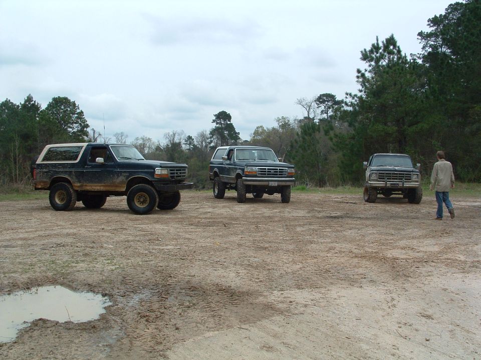 Three dark blue Ford Broncos parked in a muddy lot, one with a white top
