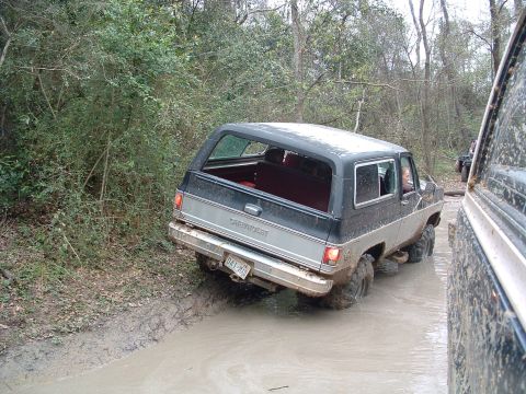 1993 Ford Bronco - A Chevrolet K5 Blazer navigates a muddy trail, with another vehicle partially visible to the right.