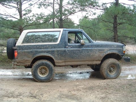 1993 Ford Bronco - This 1993 Ford Bronco is shown in profile, covered in mud and driving through a wet, wooded area.