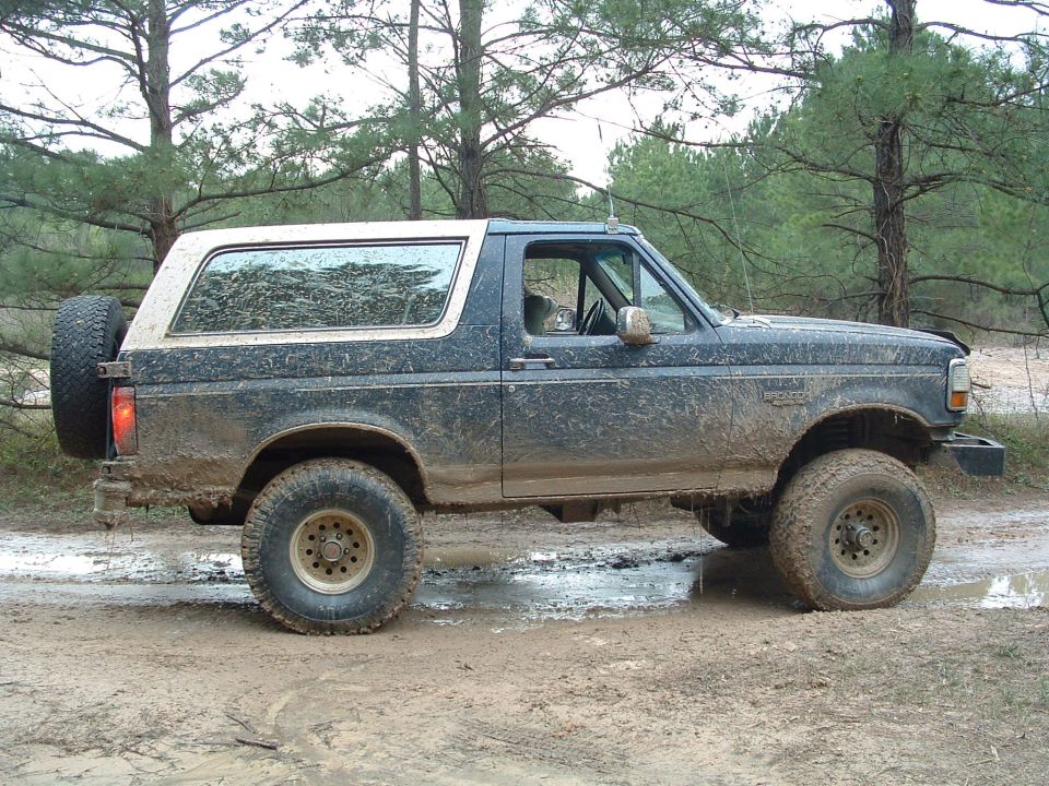 Side view of a muddy 1993 Ford Bronco with a white top and spare tire