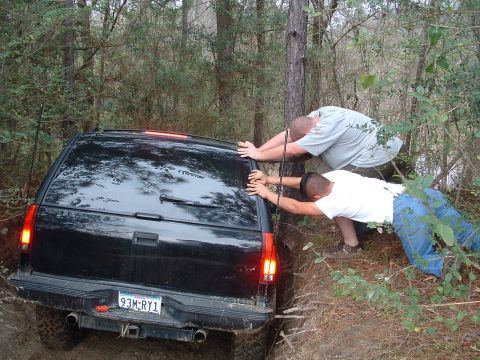 1993 Ford Bronco - Two men push a black SUV stuck in a wooded area. The license plate reads 93M-RY1.