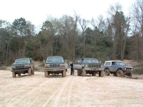 1993 Ford Bronco - Four SUVs are parked on a dirt lot with trees in the background. The registry claims one is a 1993 Ford Bronco.