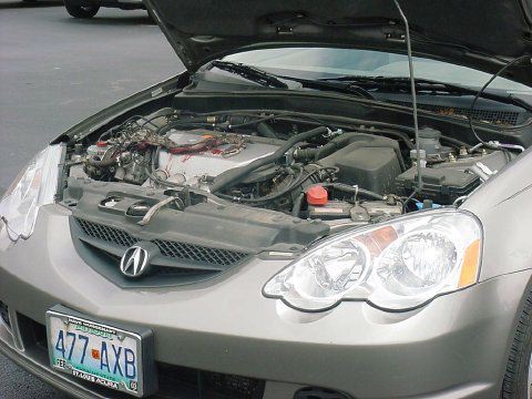 1990 Ford Bronco - open engine bay of a gray Acura coupe with the hood raised, showing the engine, headlight, and Acura grille badge.