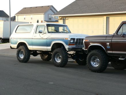 1979 Ford Bronco - A lifted 1979 Ford Bronco is parked next to a brown Ford F-Series truck in front of a garage.