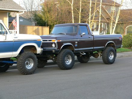 1979 Ford Bronco - A lifted brown 1979 Ford F-250 pickup truck is parked on a street next to another lifted truck.
