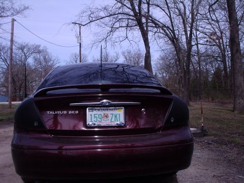 2000 Ford Taurus - The rear of a maroon 2000 Ford Taurus SES is visible, parked outdoors with trees in the background.