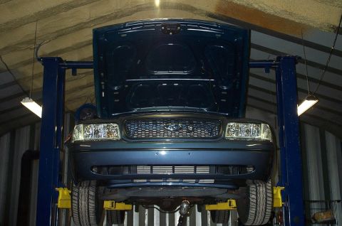 1998 Ford Crown Victoria - Front view of a dark blue Ford sedan raised on a two-post lift with its hood open, showing the grille with Ford oval, dual headlights, and…