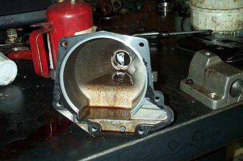 1998 Ford Crown Victoria - A cast aluminum transmission tailshaft housing sits on a workbench, showing its bolt flange, gasket surface, and a machined bearing bore wi…