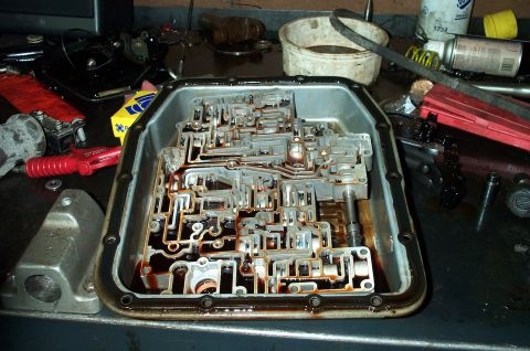 1998 Ford Crown Victoria - An automatic transmission valve body sits inside an oil-pan or housing on a workbench, its aluminum casting showing intricate fluid passage…