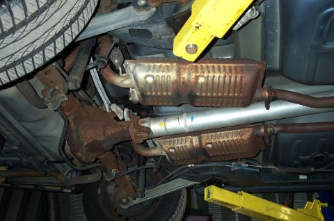 1998 Ford Crown Victoria - Undercarriage shot of an exhaust system on a lift, showing rusty pipes, dual catalytic converters and a fresh silver muffler.