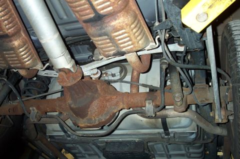 1998 Ford Crown Victoria - Undercarriage view of a vehicle's rusty rear axle, driveshaft, dual exhaust and suspension links.