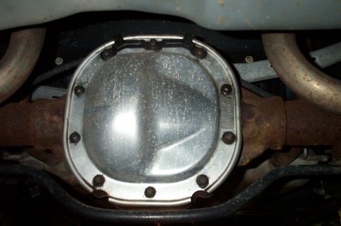 1998 Ford Crown Victoria - Underside view of a rear differential fitted with a bare metal (aluminum) cover secured by perimeter bolts, flanked by the axle tubes and r…