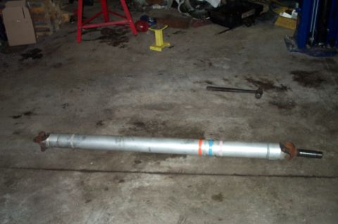 1998 Ford Crown Victoria - An aluminum driveshaft lies on a concrete garage floor, with a U-joint yoke at one end and a splined slip yoke at the other, marked with re…