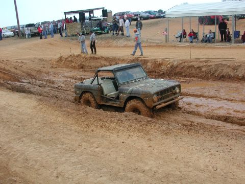 1985 Ford Bronco - This 1975 Ford Bronco is deeply stuck in a muddy track, with spectators watching from the sidelines.