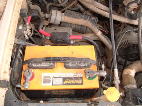 1990 Ford Bronco - Close-up view of a vehicle's engine bay, focusing on the battery and alternator.