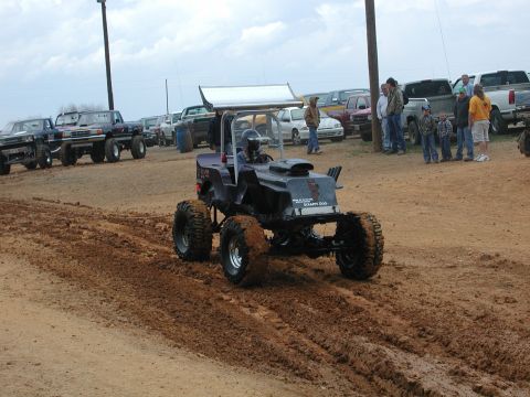 1985 Ford Bronco - A custom-built mud bogger navigates a muddy track, with spectators and other vehicles in the background.