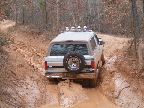 1996 Ford Bronco - A silver 1996 Ford Bronco navigates a muddy path in a wooded area.