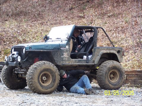 1979 Ford F-150 - A person works on the undercarriage of a modified Jeep Wrangler, while another person sits inside.