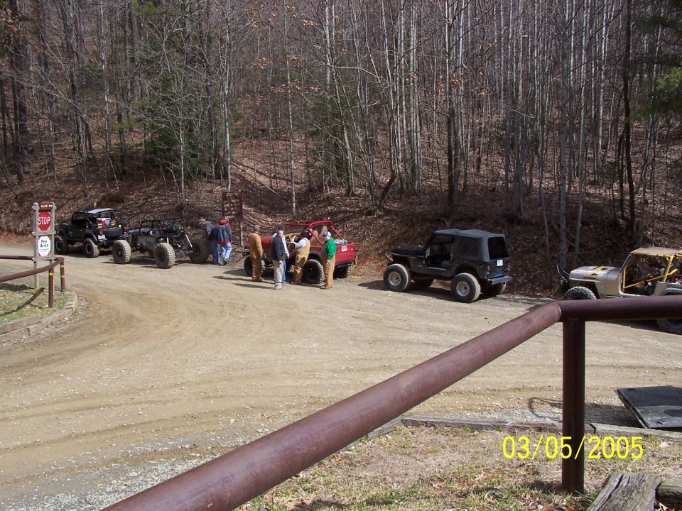 Several off-road vehicles parked on a dirt road with trees in the background