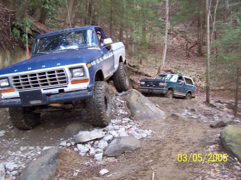 1979 Ford F-150 - Two trucks navigate a challenging off-road trail in a wooded area.