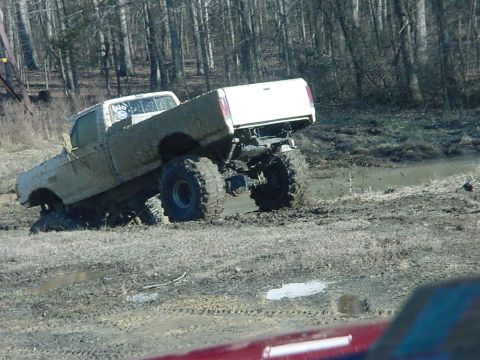 1989 Ford Bronco - This lifted pickup truck is stuck deep in the mud, its tires barely visible.