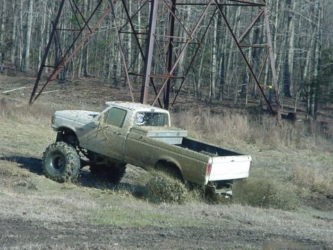 1989 Ford Bronco - A lifted pickup truck is covered in mud as it navigates a challenging off-road terrain.