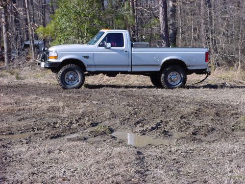 1989 Ford Bronco - This white pickup truck is parked in a muddy, wooded area.