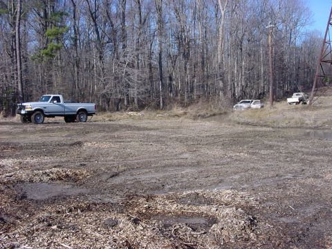 1989 Ford Bronco - Several pickup trucks are parked in a muddy, wooded area, suggesting off-road activity.
