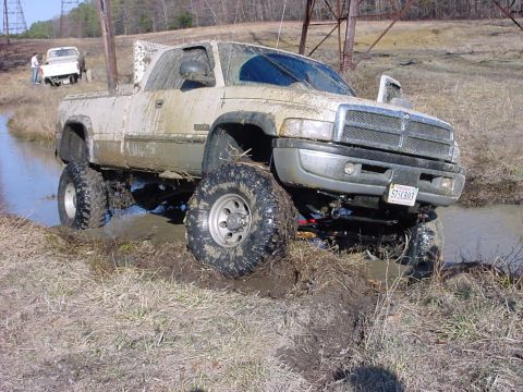 1989 Ford Bronco - A lifted pickup truck navigates a muddy off-road course, with another vehicle visible in the background.